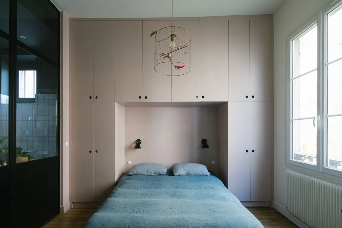 Chambre avec grand rangement sur mesure rose poudré encadrant la tête de lit, suspension en cage dorée et verrière noire