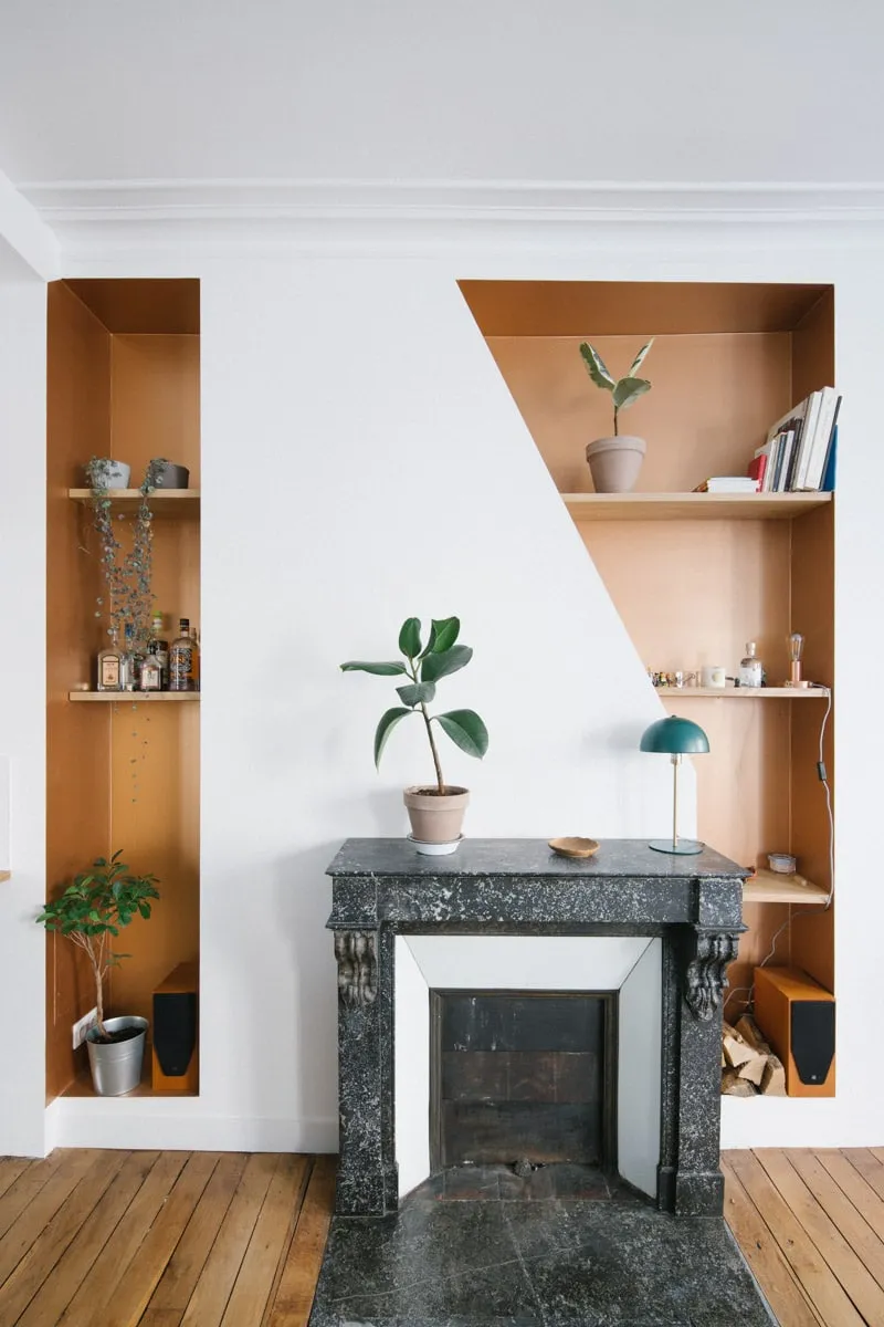Salon parisien rénové avec deux niches murales sur mesure de part et d’autre d’une cheminée en marbre noir