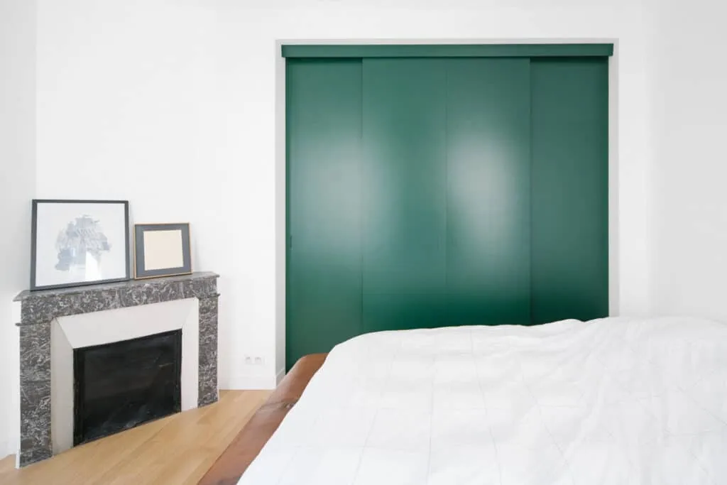 Chambre rénovée avec placard encastré à portes coulissantes vertes, cheminée d’angle en marbre gris et parquet clair