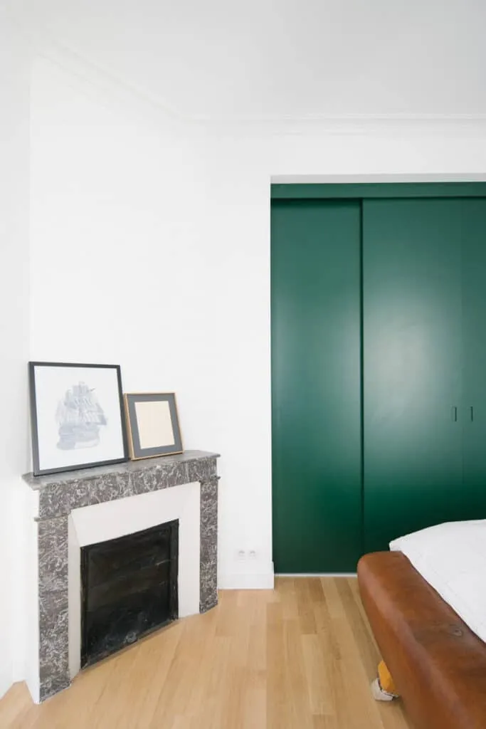 Chambre rénovée avec placard sur mesure à portes coulissantes vertes, cheminée d’angle en marbre gris et parquet clair