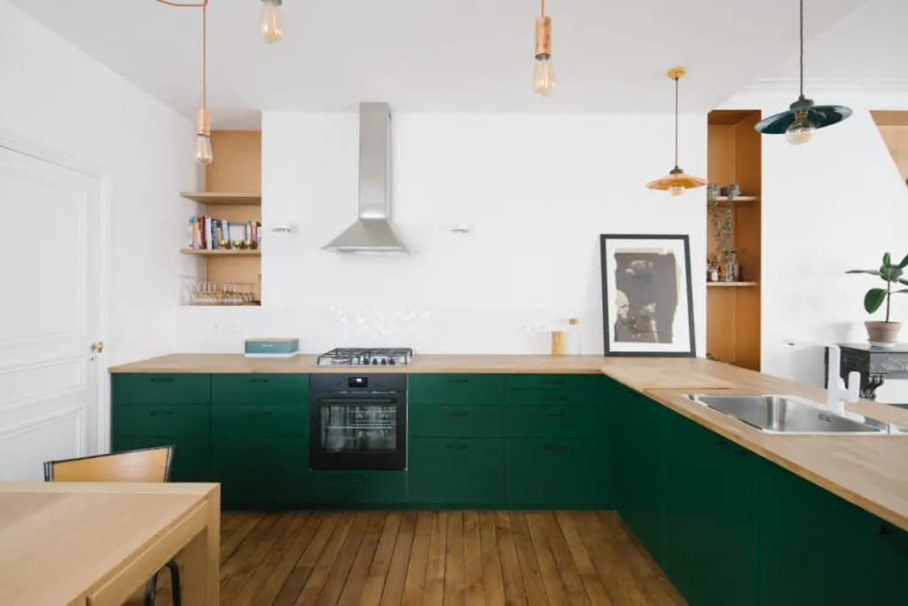 Cuisine rénovée avec meubles verts, plan de travail en bois, hotte inox et niches en bois dans un appartement lumineux