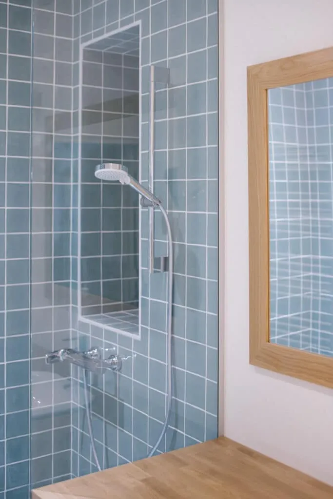Douche rénovée avec carrelage bleu-gris, niche encastrée, robinetterie chromée et miroir à cadre en chêne