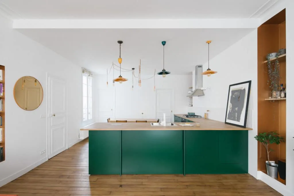 Cuisine ouverte avec îlot en bois et façades vert foncé, suspensions colorées, parquet ancien et niche murale sur mesure