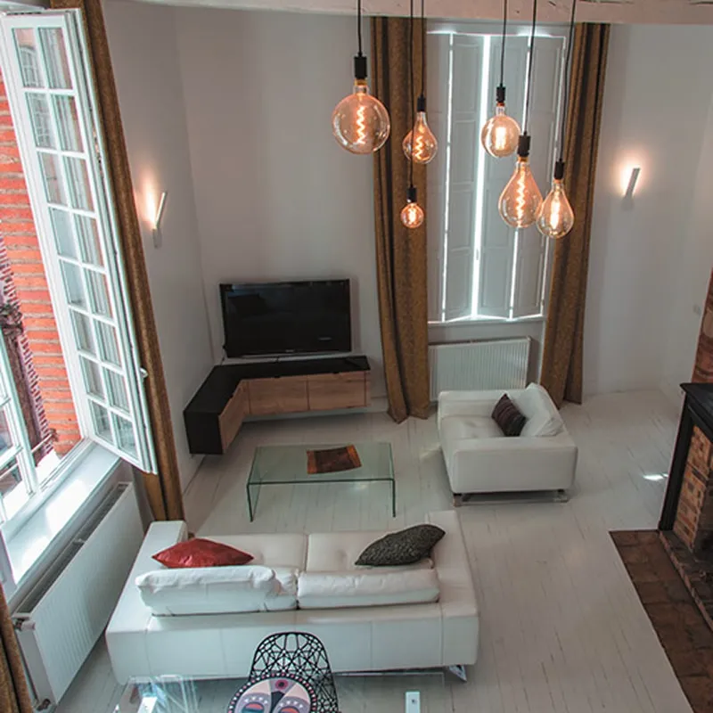 Salon en hauteur sous plafond avec suspensions à ampoules design, canapés blancs et meuble TV suspendu en bois