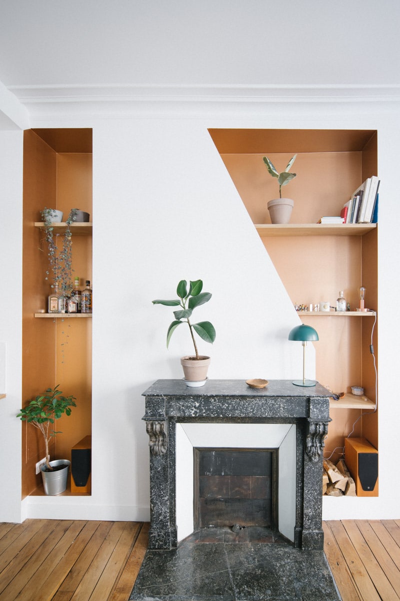 Cheminée en marbre noir entre deux niches étagères cuivrées, décorées de plantes vertes et d'objets.